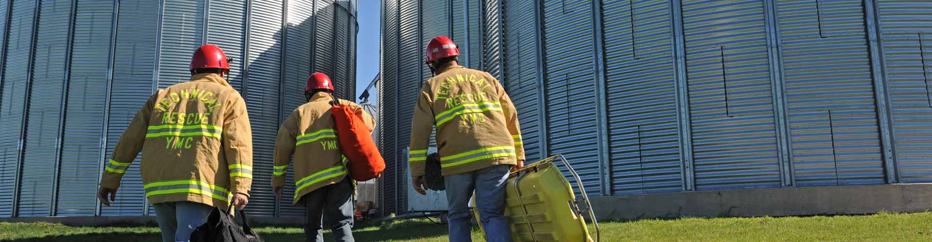 Three firefighters walking towards grain bins with safety gear